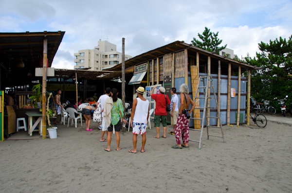 <b>海沿いの道を歩いているとヘンテコリンな建物を見つけた。「へんな建物は何?」って後できいたらココは個人所有の地元の仲間が集まる場所らしく、これもブルースさんが作ったスイカのオブジェだった(笑)。神社にある橋を越えたらオアシスへ到着。現場にはブルースさんの仲間のカメラマンが集まっていた。右写真:左側はミュージシャンを数多く撮っている仁礼博さん、ブルースの右側は日本に於けるサーフィン写真界の第一人者、横山泰介さん。地元の不良オヤジではなくて(失礼!笑)、個性的なおじさんたちだが、そのうちココで登場して頂きたいくらい有名な写真家の先輩たちだ</b>