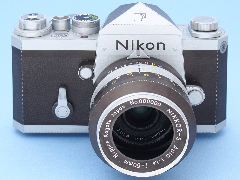一見すると、フィルム一眼レフの名機「ニコンF」なのだが、実は中身は最新のデジカメで、もちろん撮影可能である。外装はホンモノのニコンFではなく、ニコンダイレクト限定グッズの「ニコンFペーパークラフト」で、つまり素材は紙である。その紙のニコンFに、ホンモノのデジカメ「Nikon1 V3」を内蔵し、さらに電源スイッチやシャッターボタンを操作する機構も組み込んだ。これらのパーツ類も、今回は全て紙で製作した。レンズは「1 NIKKOR 18.5mm f/1.8」を装着し、ニコンFペーパークラフトのレンズNikkor 50mm F1.4と同様の画角で撮影できる。