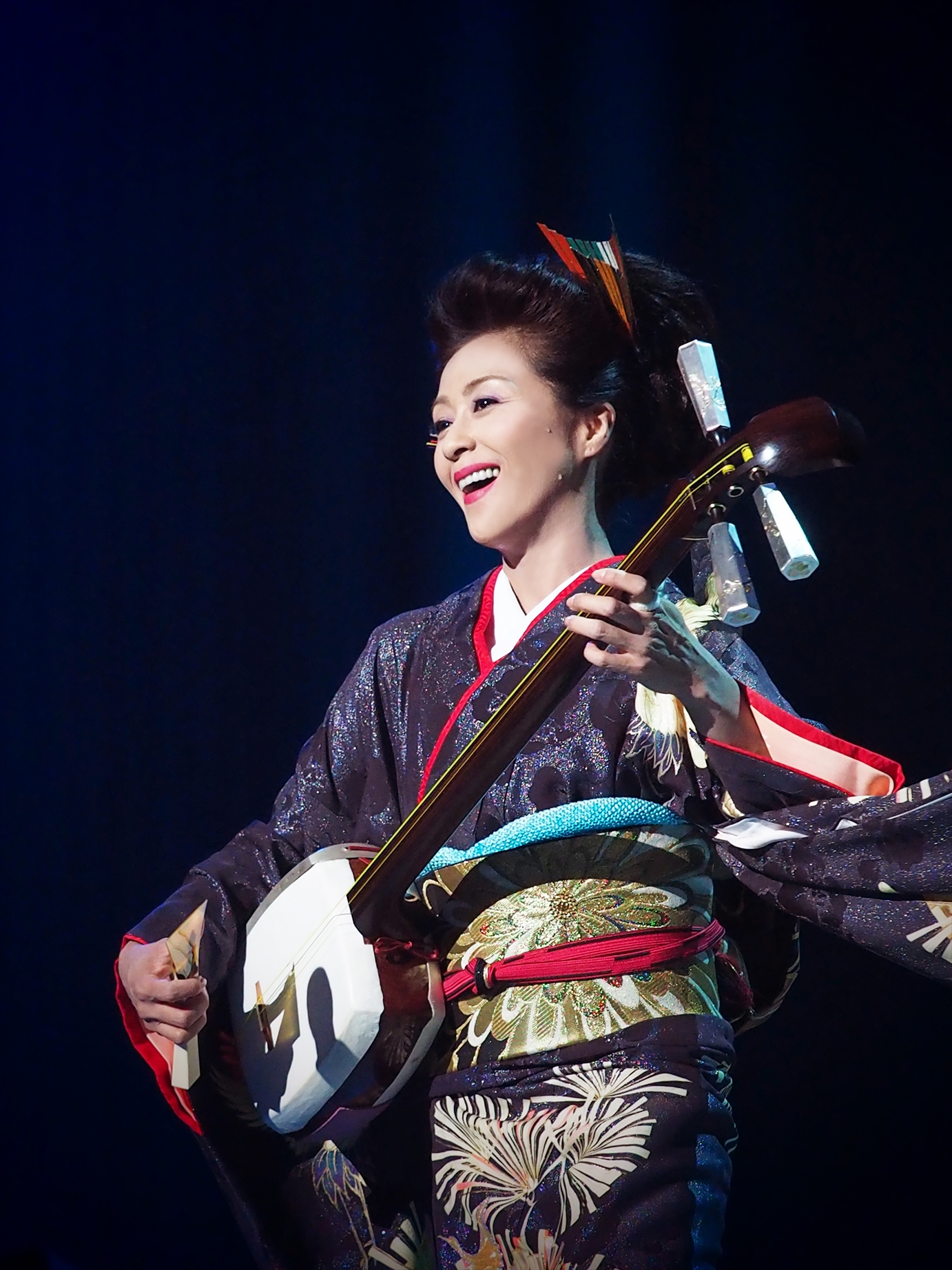 長山洋子さんの「じょんから女節」歌唱中の一枚。この楽曲は長山さんの演歌の中でもロック色の強い作品。激しいリズムで津軽三味線を立ち弾きしながら長い振袖を揺らし、渾身の歌唱とパフォーマンスが続くため、ダンサーやアスリートを撮るのと同じくらいの緊張感で撮っています。このカットは歌の合間にクルリと回った瞬間、キラリと流れる大粒の汗と爽やかな笑顔を捉えることができました。<br><span class="fnt-85">オリンパス OM-D E-M1 / M.ZUIKO DIGITAL ED 40-150mm F2.8 PRO / 46mm(92mm相当)/絞り優先AE(F3.5、1/800秒、±0EV)/ ISO 1600</span>